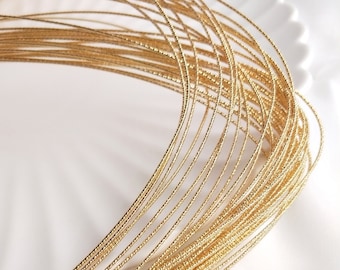May include: A close-up of a bundle of gold-colored wire. The wire is thin and has a textured surface.
