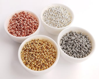 May include: Four white bowls filled with small round beads. The bowls are arranged in a circle. The beads are gold, silver, rose gold, and black.