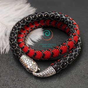 May include: A beaded snake necklace with a silver snake head clasp. The snake is made of black and red beads, creating a striking pattern.