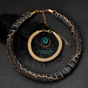 Può includere: Un set di collana e braccialetto in perle dorate e nere. La collana ha un motivo geometrico e il braccialetto è in oro massiccio.