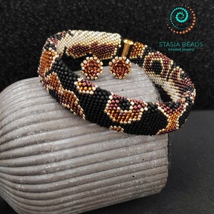 May include: A beaded bracelet and matching earrings in a geometric pattern with black, brown, gold, and white beads. The jewelry is displayed on a gray textured surface.