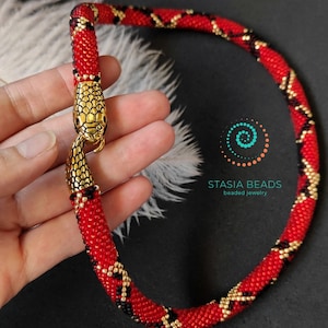 May include: Red and black beaded snake necklace with a gold snake head clasp. The necklace is made with small beads and has a geometric pattern.