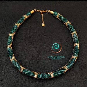Puede incluir: Un collar de cuentas verde y dorado con un patrón geométrico. El collar está hecho de cuentas pequeñas y redondas y tiene un cierre dorado.