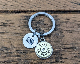 May include: A silver key chain with two charms. One charm is a silver circle with a small American flag design. The other charm is a gold-colored bullet casing with the text "44 REM MAG USA" printed on it.