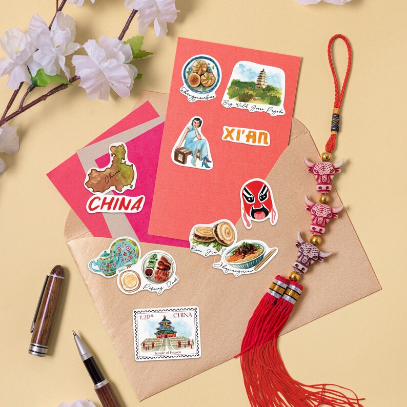 May include: A set of colorful stickers featuring images of Chinese landmarks, food, and culture. The stickers are arranged on a red and brown envelope with a red tassel hanging from the top. The stickers include a map of China, a pagoda, a traditional Chinese mask, a bowl of noodles, and a teapot.