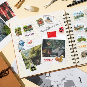 May include: A travel journal with a variety of colorful stickers and photos of China. The stickers include images of landmarks, traditional Chinese art, and the Chinese flag. The journal is open to a page with a photo of a traditional Chinese street scene.