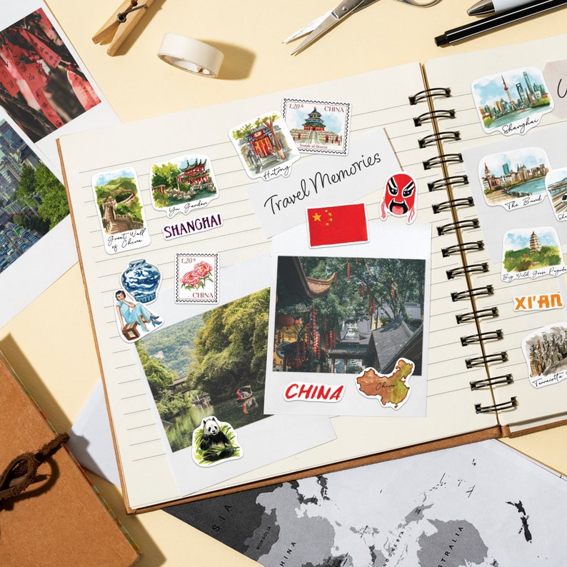 May include: A travel journal with a variety of colorful stickers and photos of China. The stickers include images of landmarks, traditional Chinese art, and the Chinese flag. The journal is open to a page with a photo of a traditional Chinese street scene.