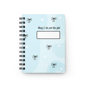 May include: A spiral-bound notebook with a light blue cover featuring black bow and heart illustrations. The text "Stuff I do for the plot" is printed above a rectangular blank space. The notebook has a black spiral binding.