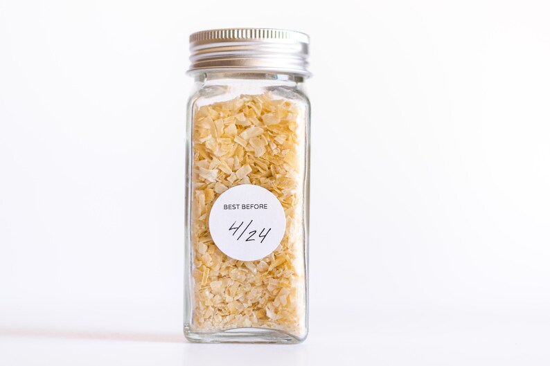 May include: A glass jar with a silver lid filled with dehydrated onion flakes. A white label on the jar reads "BEST BEFORE 4/24".