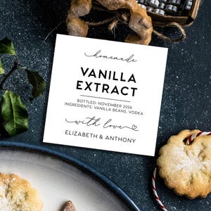 May include: A square white label with black text reading homemade VANILLA EXTRACT, BOTTLED: NOVEMBER 2026, INGREDIENTS: VANILLA BEANS, VODKA, with love, and ELIZABETH & ANTHONY. The label features a script font for homemade and with love.