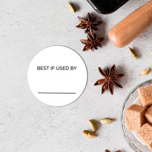 May include: White round sticker with the text "BEST IF USED BY" printed in black. The sticker is on a white background with brown star anise and cardamom pods.