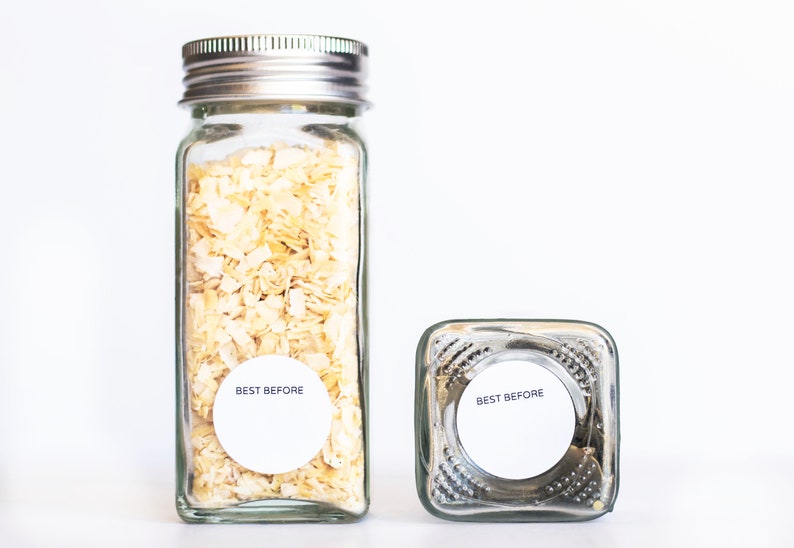 May include: Two glass jars with silver lids. The jars are filled with dried onion flakes. Both jars have white round labels that say "Best Before" on them.