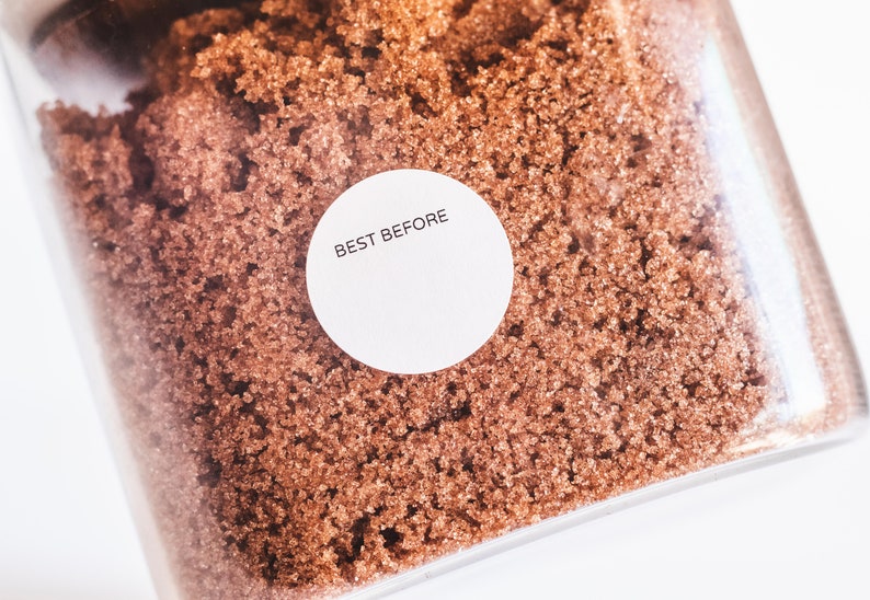 May include: A close-up of a clear container filled with brown sugar. A white round label with the text "BEST BEFORE" is attached to the container.