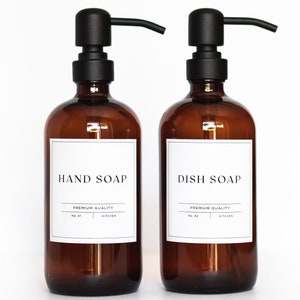 May include: Two amber glass bottles with black pump tops and white labels. The labels read "HAND SOAP" and "DISH SOAP" with the text "PREMIUM QUALITY KITCHEN" underneath.