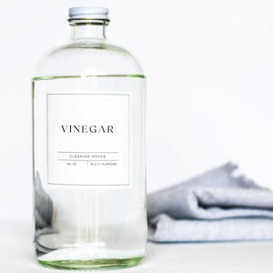 May include: A clear glass bottle with a white label that reads "Vinegar Cleaning Grade No. 01 Multi-Purpose". The bottle is sitting on a white surface with a gray cloth folded in the background.