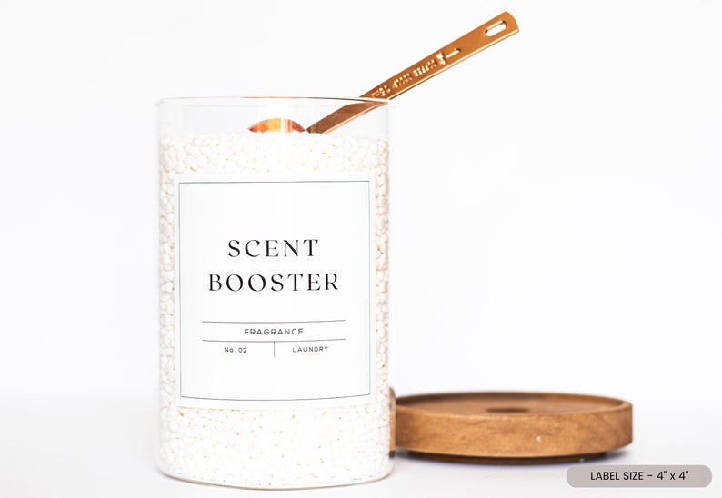 May include: A clear glass jar filled with white laundry scent booster beads. The jar has a white label with black text that reads "SCENT BOOSTER", "FRAGRANCE", "NO. 02", and "LAUNDRY". A gold metal spoon is resting on the top of the jar.