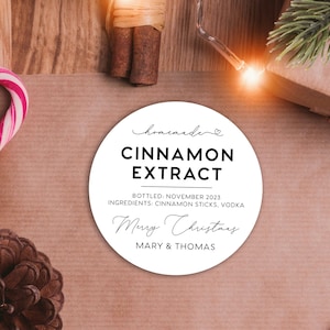 May include: A round white label with black text that reads: homemade CINNAMON EXTRACT BOTTLED: NOVEMBER 2023 INGREDIENTS: CINNAMON STICKS, VODKA Merry Christmas MARY & THOMAS. The label features a small heart icon above the word homemade.