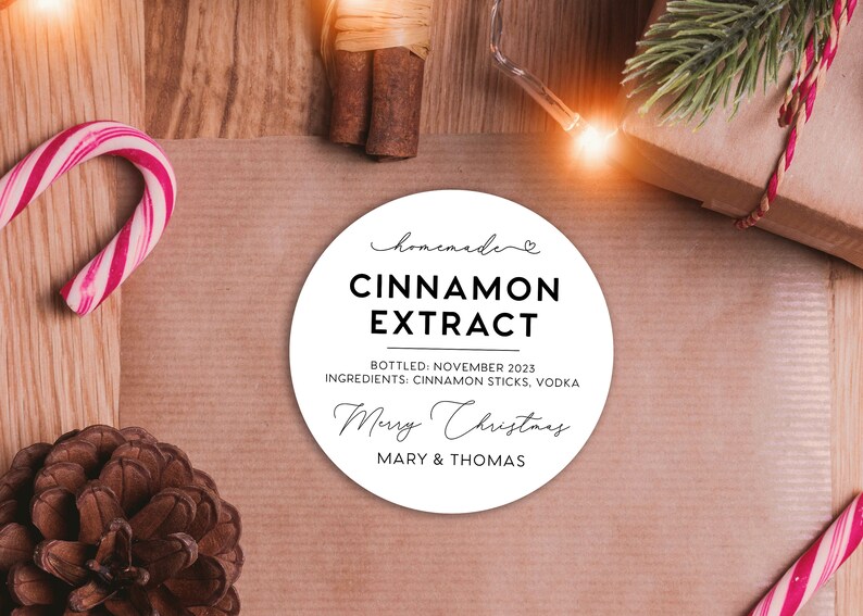 May include: A round white label with black text that reads: homemade CINNAMON EXTRACT BOTTLED: NOVEMBER 2023 INGREDIENTS: CINNAMON STICKS, VODKA Merry Christmas MARY & THOMAS. The label features a small heart icon above the word homemade.