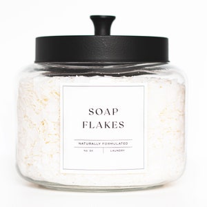 May include: A glass jar with a black lid filled with white soap flakes. The jar has a label that reads "SOAP FLAKES NATURALLY FORMULATED NO. 04 LAUNDRY".