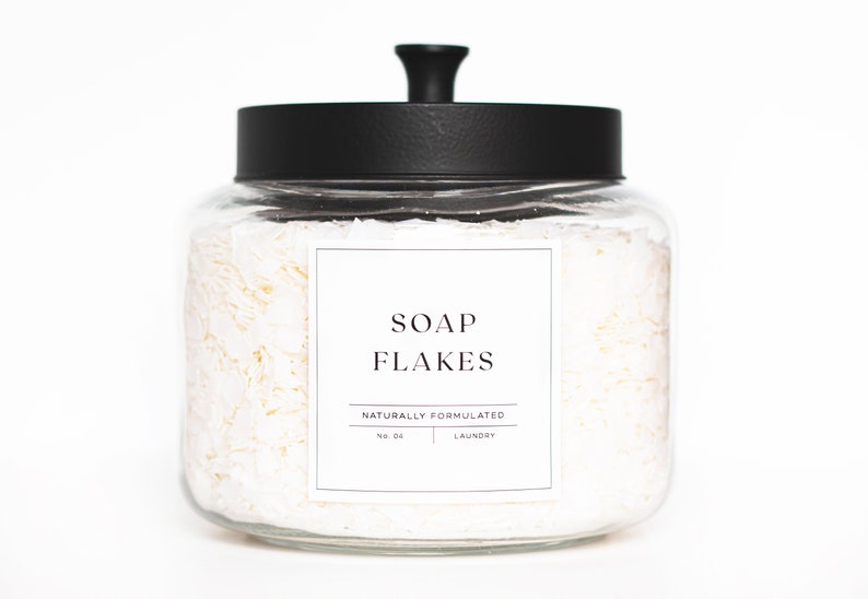 May include: A glass jar with a black lid filled with white soap flakes. The jar has a label that reads "SOAP FLAKES NATURALLY FORMULATED NO. 04 LAUNDRY".