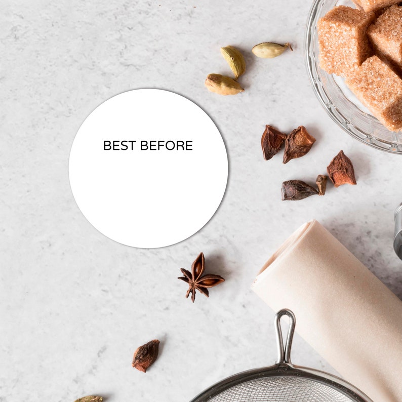 May include: A white circle with the text 'BEST BEFORE' on a white marble surface. There are brown star anise, green cardamom pods, and brown sugar cubes in the background.