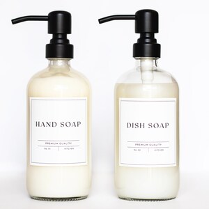 May include: Two clear glass bottles with black pump tops and white labels. The labels read "HAND SOAP" and "DISH SOAP" with the text "PREMIUM QUALITY" underneath.