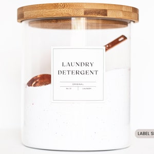 May include: A glass jar with a bamboo lid filled with white laundry detergent. A copper measuring spoon is inside the jar. A white label on the jar reads "Laundry Detergent" with the words "Original" and "No. 01 Laundry" underneath. The label is 3 inches by 3 inches.