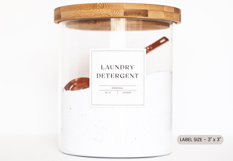 May include: A glass jar with a bamboo lid filled with white laundry detergent. A copper measuring spoon is inside the jar. A white label on the jar reads "Laundry Detergent" with the words "Original" and "No. 01 Laundry" underneath. The label is 3 inches by 3 inches.