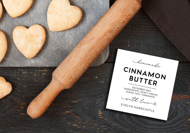 May include: A wooden rolling pin, heart-shaped cookies on a gray board, and a white square label that reads: homemade CINNAMON BUTTER DECEMBER 2023 INGREDIENTS: HEAVY CREAM, SUGAR, SALT, CINNAMON with love EVELYN HARDCASTLE.