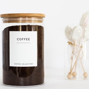 Pu&ograve; includere: Un barattolo di vetro con un coperchio in bamb&ugrave; pieno di fondi di caff&egrave;. Il barattolo ha un'etichetta bianca con la parola "COFFEE" e il testo "COFFEE COLLECTION" stampato su di essa.