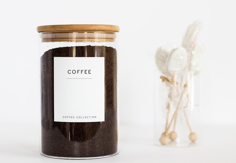 Pu&ograve; includere: Un barattolo di vetro con un coperchio in bamb&ugrave; pieno di fondi di caff&egrave;. Il barattolo ha un'etichetta bianca con la parola "COFFEE" e il testo "COFFEE COLLECTION" stampato su di essa.