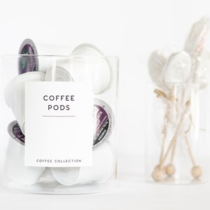 Pu&ograve; includere: Un barattolo di vetro trasparente pieno di capsule di caff&egrave; bianche. Il barattolo ha un'etichetta bianca che dice "COFFEE PODS" e "COFFEE COLLECTION".