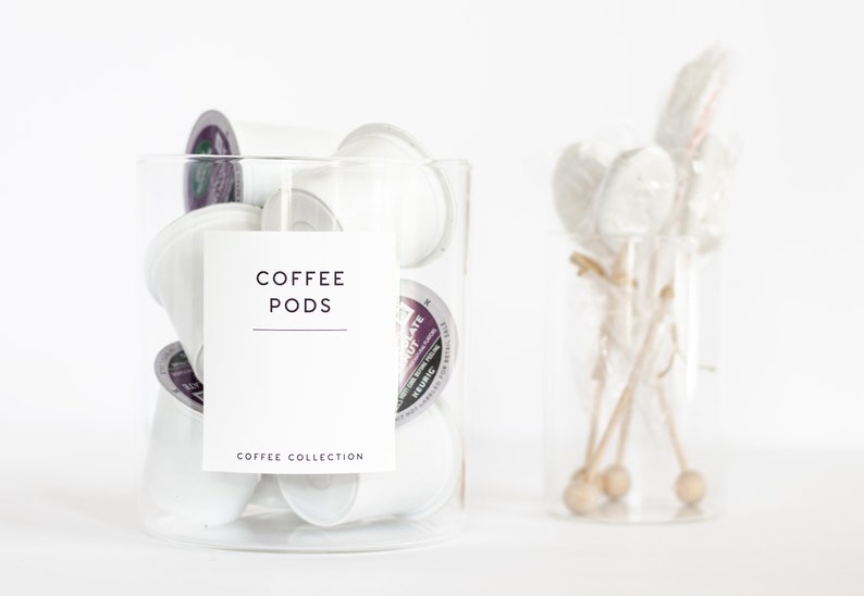 Pu&ograve; includere: Un barattolo di vetro trasparente pieno di capsule di caff&egrave; bianche. Il barattolo ha un'etichetta bianca che dice "COFFEE PODS" e "COFFEE COLLECTION".
