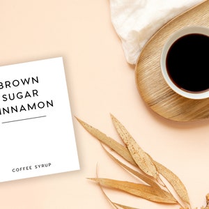 Pu&ograve; includere: Un biglietto bianco con il testo "BROWN SUGAR CINNAMON COFFEE SYRUP" su uno sfondo rosa chiaro con una tazza di caff&egrave;, foglie secche e un panno bianco.