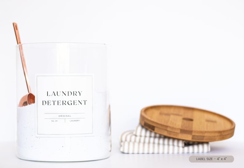 May include: A clear glass jar with a white lid and a white label that says "Laundry Detergent" with a copper scoop inside. The jar is sitting on a white surface. The label size is 4" x 4".