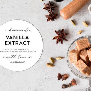 May include: A round white label with black text reading homemade VANILLA EXTRACT, BOTTLED: OCTOBER 2023, INGREDIENTS: VANILLA BEANS, WHISKEY, with love, and MARIANNE. Nearby are star anise, cardamom pods, and a glass bowl filled with brown sugar cubes.