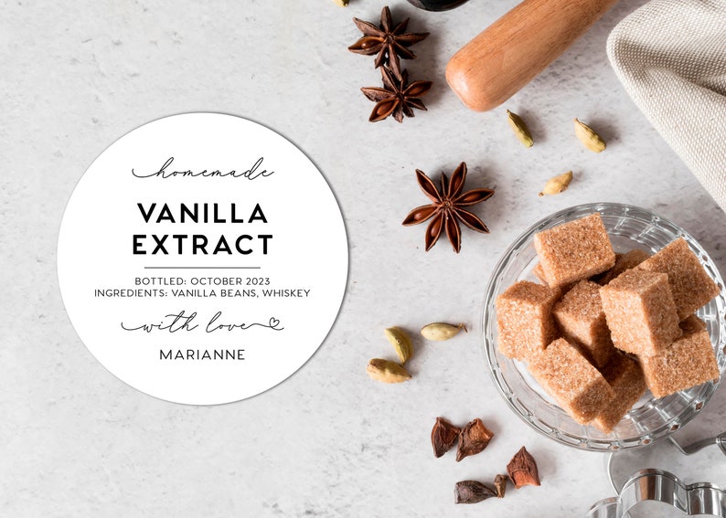 May include: A round white label with black text reading homemade VANILLA EXTRACT, BOTTLED: OCTOBER 2023, INGREDIENTS: VANILLA BEANS, WHISKEY, with love, and MARIANNE. Nearby are star anise, cardamom pods, and a glass bowl filled with brown sugar cubes.