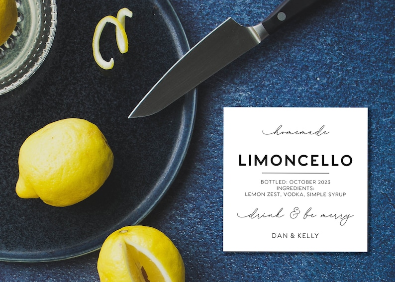 May include: A white square label with black text reading homemade LIMONCELLO, BOTTLED: OCTOBER 2023, INGREDIENTS: LEMON ZEST, VODKA, SIMPLE SYRUP, drink & be merry, DAN & KELLY, placed near two yellow lemons, a lemon peel, and a kitchen knife.