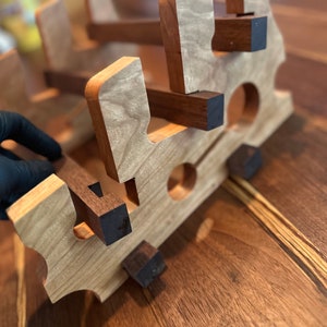 Puede incluir: Un estante de vino de madera con un acabado de madera natural y detalles en marrón oscuro. El estante está diseñado para contener varias botellas de vino.