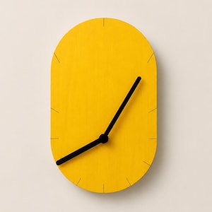 May include: An oval-shaped wall clock with a bright yellow face and a smooth, matte finish. The clock features thin, black tick marks for the hour indicators and two black hands pointing to the time. The design is simple, clean, and functional.