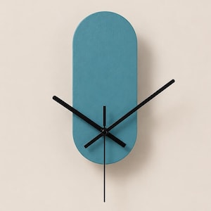 May include: A wall clock with a vertical, pill-shaped teal face and four thin, black metal hands. The clock face has a smooth, matte finish and lacks any numbers or hour markers, featuring a simple, clean design with a central black mechanism.