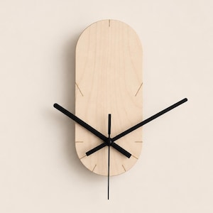 Könnte beinhalten: Eine vertikale, ovale Wanduhr aus hellem Holz mit glatter Maserung. Das Zifferblatt weist feine, eingravierte Linien zur Stundenmarkierung auf sowie drei schlanke, schwarze Zeiger, die mittig angebracht sind, um die Zeit anzuzeigen.