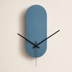 May include: A wall clock with a vertical pill-shaped face in a matte dusty blue finish. The clock features thin black hour, minute, and second hands centered on the face. Small, subtle black tick marks are etched along the rounded edges.