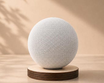 Könnte beinhalten: Ein weißer, kugelförmiger Lautsprecher mit strukturierter Oberfläche, der auf einem kleinen, runden Holzständer steht. Der Hintergrund ist ein neutrales Beige, mit Schatten von Blättern. Das Design ist minimalistisch und modern.