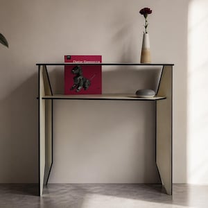Peut inclure: Une console moderne et minimaliste avec un cadre noir et des panneaux clairs. Un album rouge, un petit vase avec une fleur rouge et un haut-parleur intelligent sont sur les étagères. La table est dans une pièce aux tons neutres.