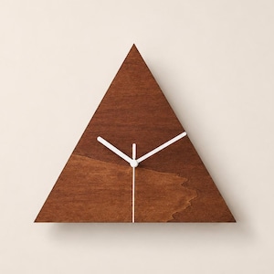 Peut inclure: Une horloge murale triangulaire en bois brun foncé avec un grain naturel visible. L'horloge présente trois fines aiguilles blanches positionnées au centre, pointant vers les bords de la face triangulaire en bois sans aucun chiffre.