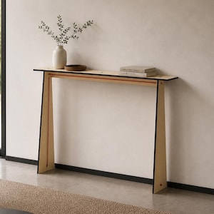 May include: A contemporary console table with a light wood finish and black edging. The table features a rectangular top and angled legs. A white vase with foliage, a small wooden bowl, and two books are displayed on the table.