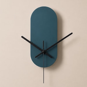May include: A wall clock featuring a solid, matte teal blue oval face with rounded ends. The clock has three thin, black metal hands positioned at the centre, with no numbers or markings on the face to indicate the time on the dial.