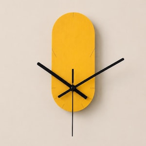 May include: A vertical oval wall clock with a bright yellow face. The clock features thin black hour, minute, and second hands centered on the face. Small black tick marks are etched into the yellow surface at the twelve, three, six, and nine o'clock positions to indicate the time. The design is simple and functional.