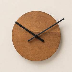 May include: A circular wall clock with a medium brown wood grain face. The clock features thin, black, straight hour and minute hands and a thin black second hand. Small, simple black tick marks are etched around the perimeter to indicate hours.